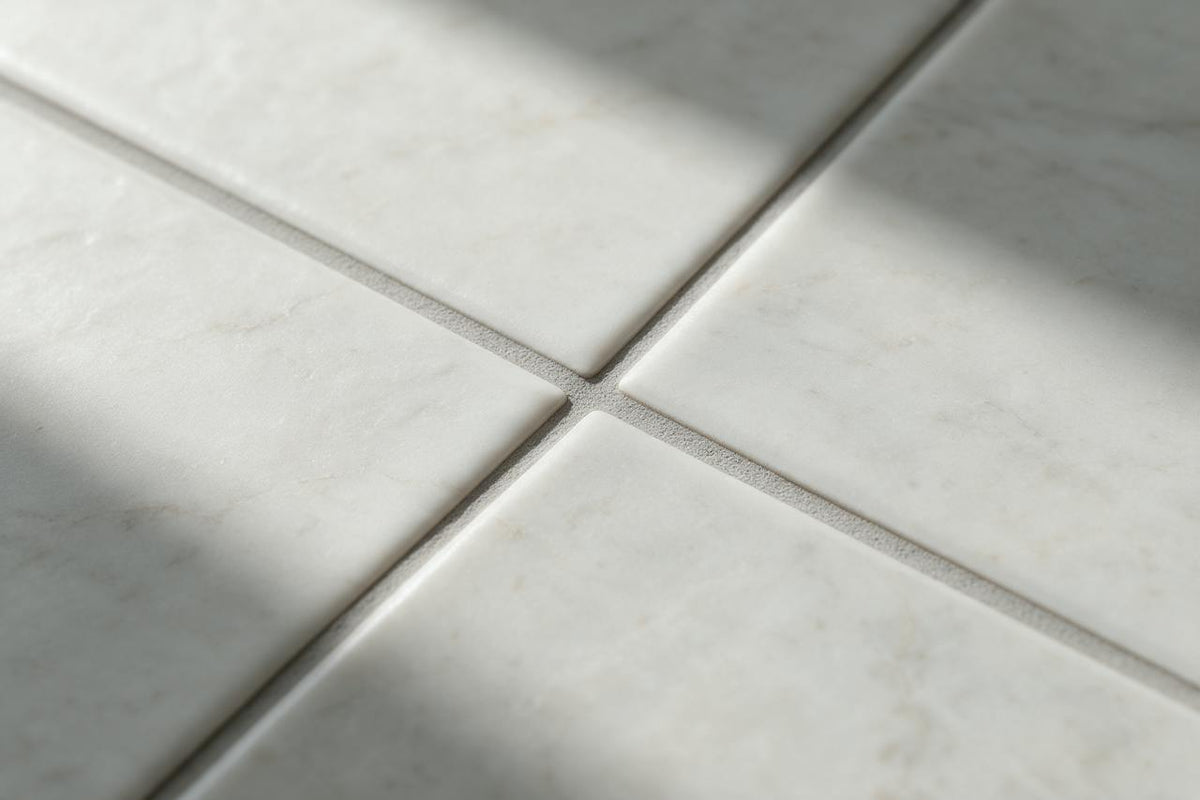 Illustrative close-up of light-coloured tiles with intersecting grey grout joints.