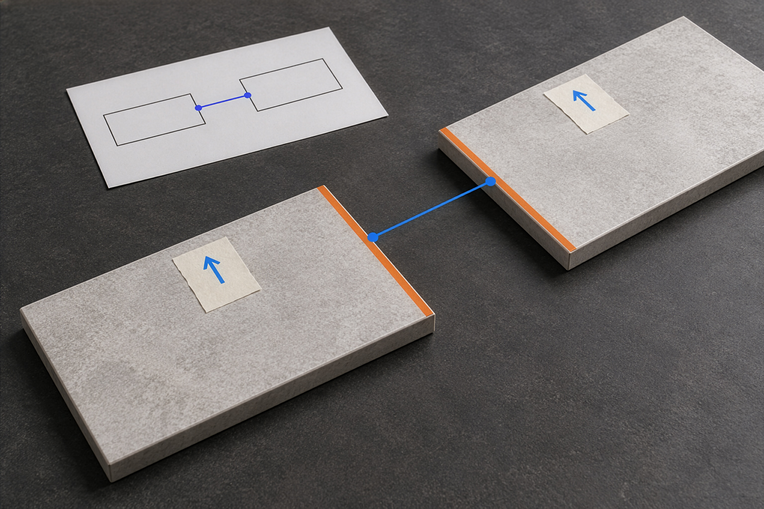 Two loose pieces with raw square edges lie separately. The orange edges are linked by a blue line as the identified pair, and taped arrows show the installed direction. The far piece is cropped by the frame; no completed corner and no cutting procedure is shown.